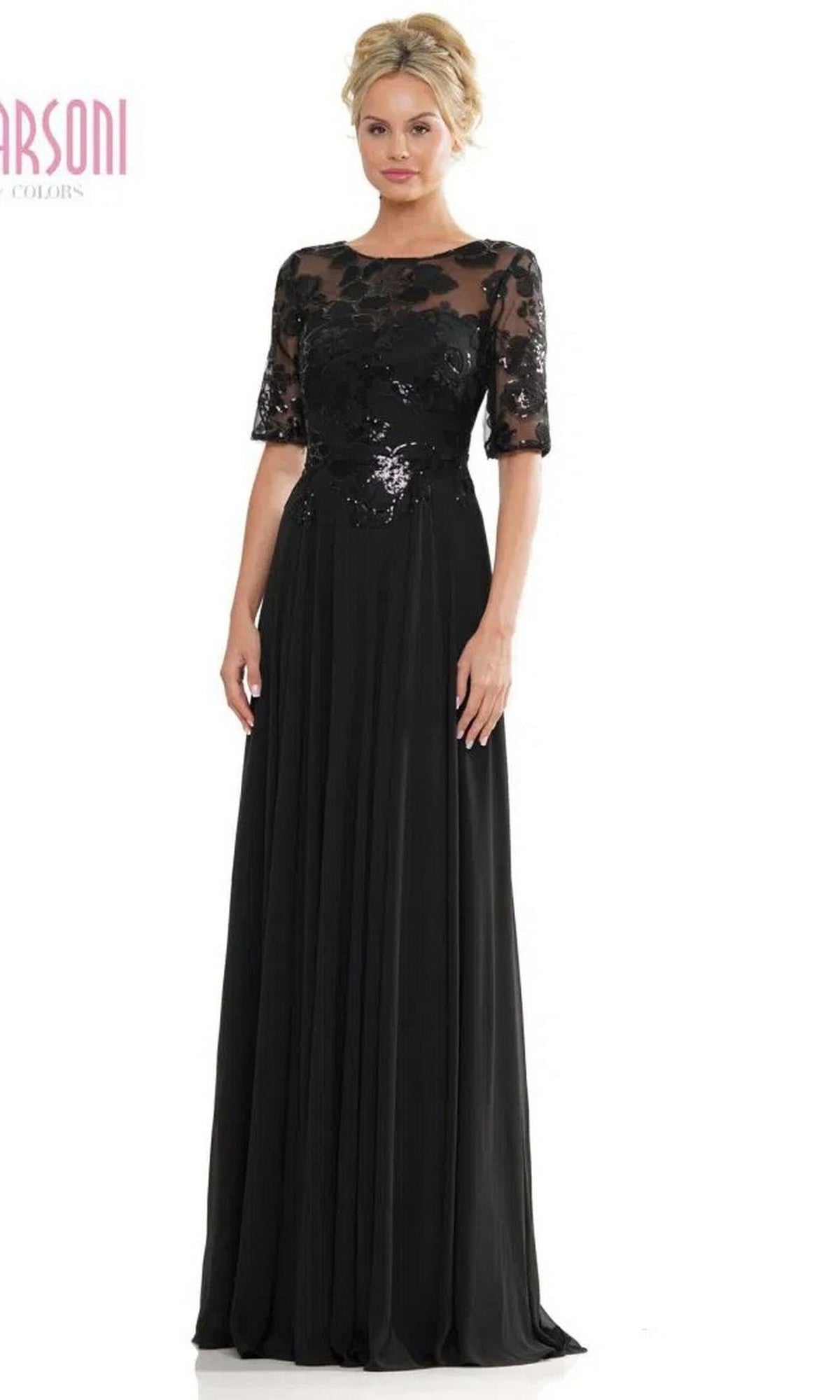 A woman models the Marsoni M286 long formal dress in black, featuring a sequin lace bodice, sheer short sleeves, and floral details on a floor-length A-line chiffon skirt, photographed against a plain white background.